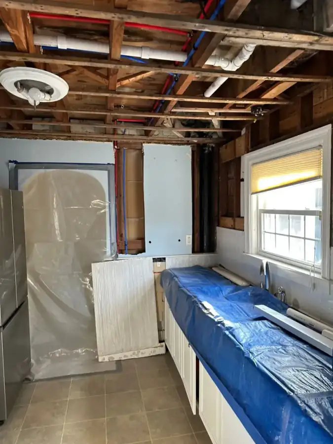 Kitchen mid demolition with exposed ceiling joists, plumbing and containment sheeting
