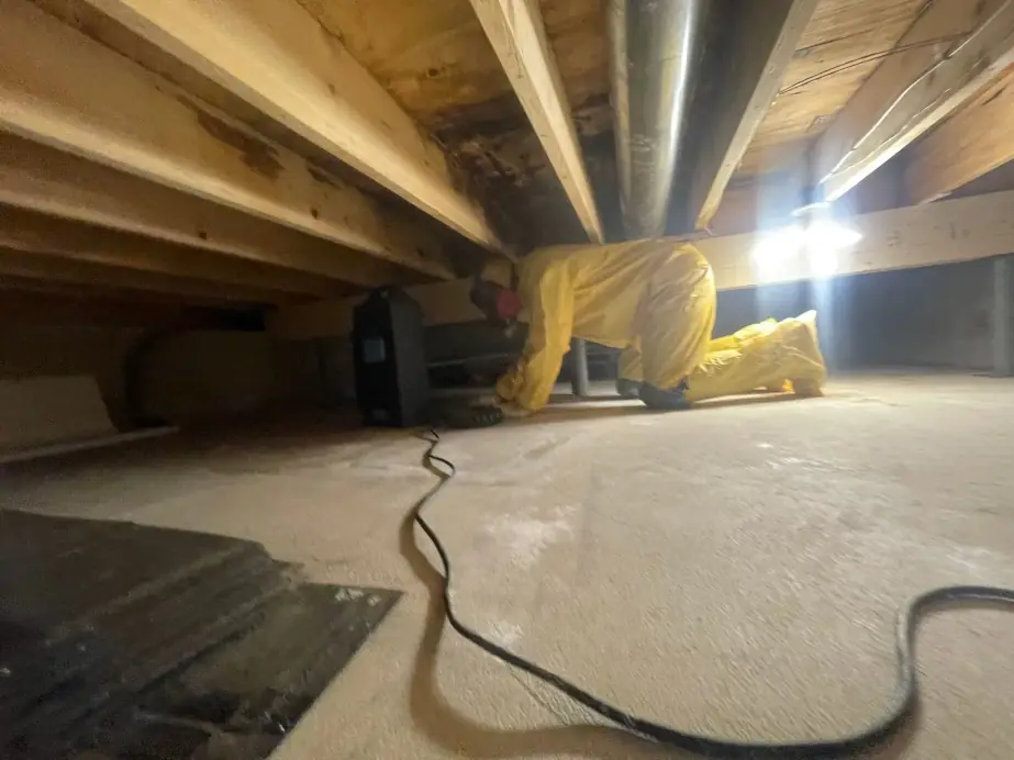 Clean Care technician in yellow protective coveralls working in a crawlspace beside HVAC ductwork