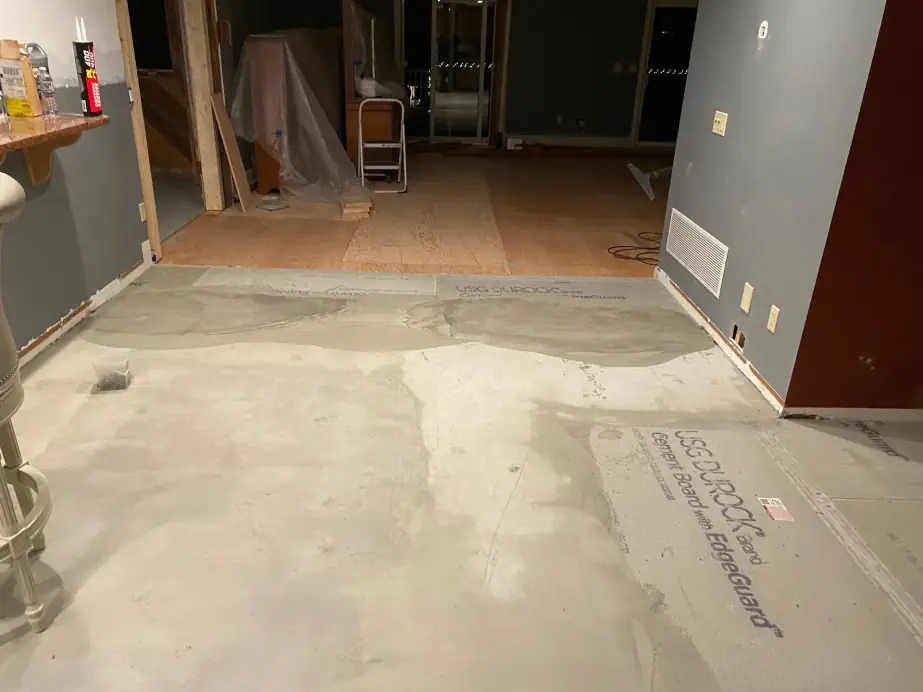 Basement floor reconstruction with cement backer board being laid over a plywood subfloor