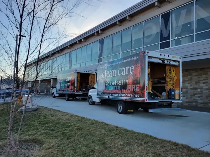 Two branded Clean Care box trucks parked outside a large commercial building