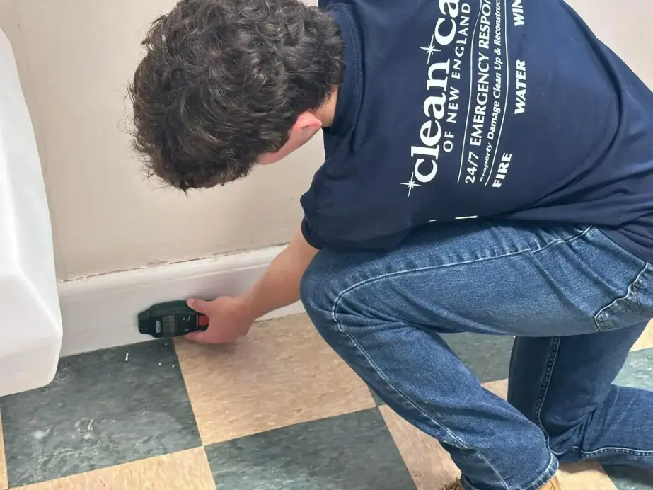 Technician reading a moisture meter against a baseboard on a vinyl floor