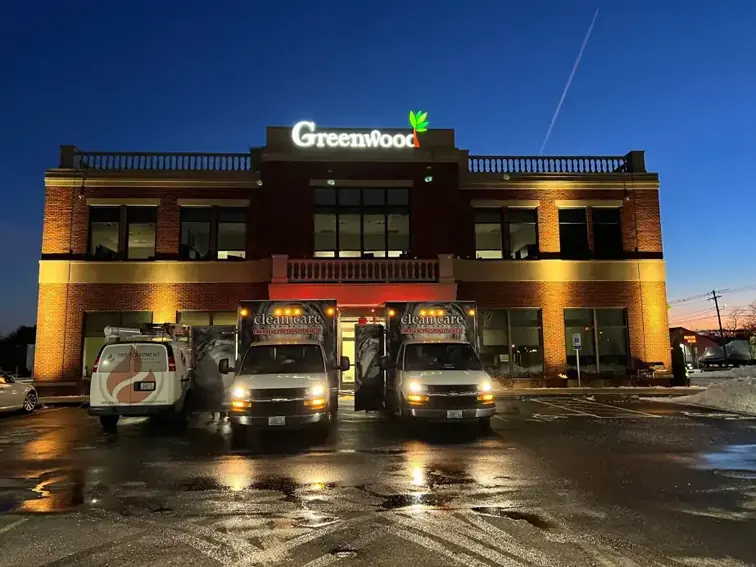 Two Clean Care of New England response trucks parked outside a commercial building at dusk