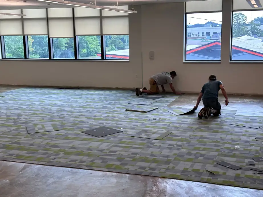 Two technicians installing carpet tile in a large open plan office