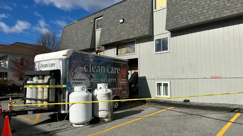 Fire damaged apartment building with boarded windows and a Clean Care equipment trailer parked outside