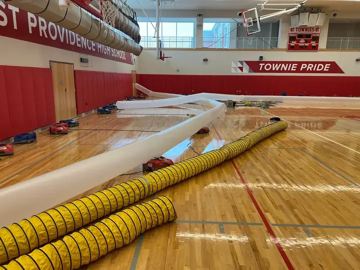 Air movers and drying ducting deployed across a high school gymnasium floor by Clean Care of New England