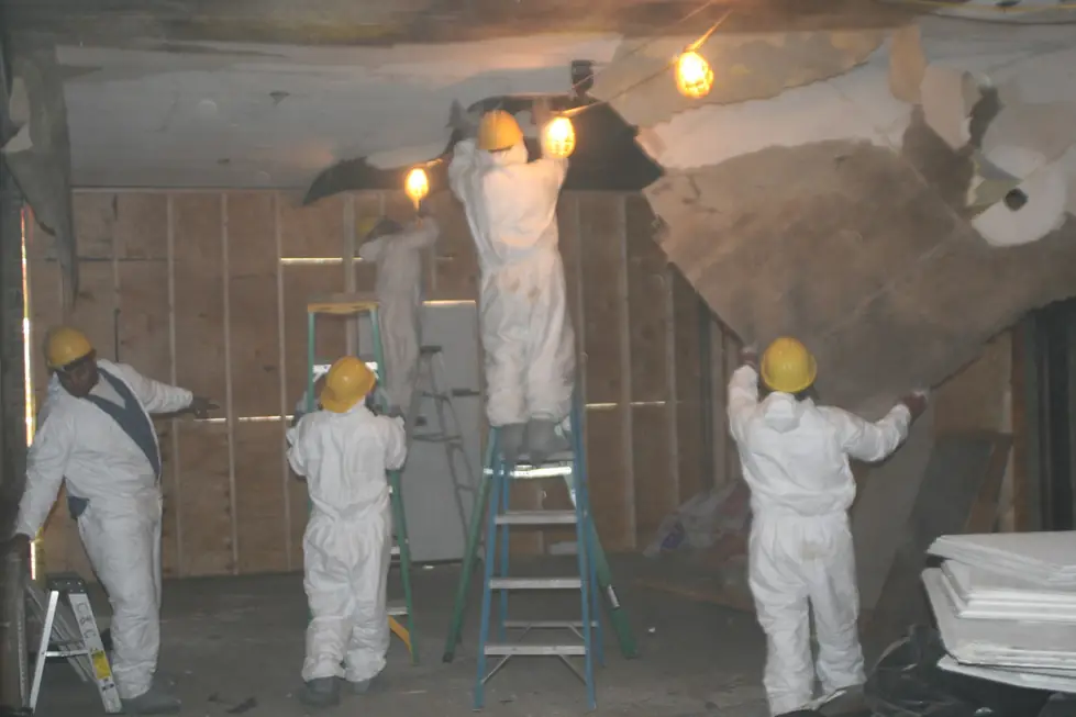 Five technicians in protective coveralls and hardhats gutting a damaged interior down to the studs
