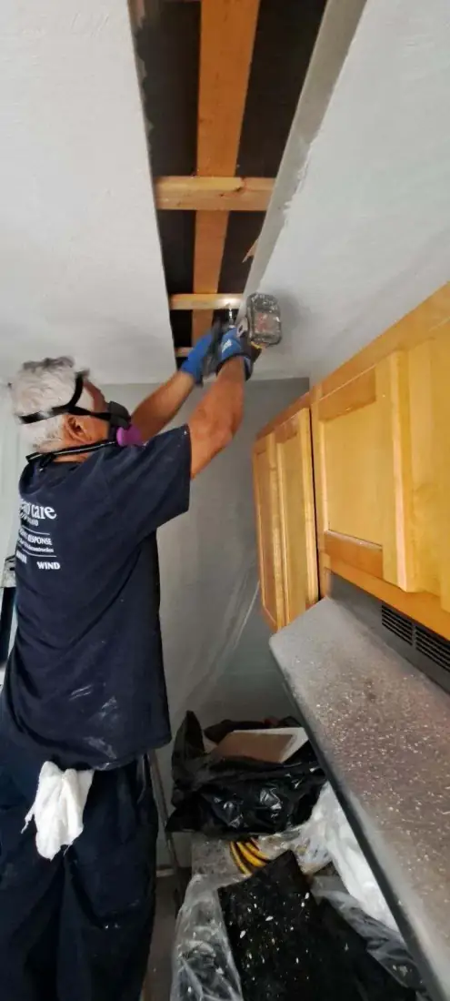 A Clean Care crew member in a Clean Care t-shirt repairing a kitchen ceiling
