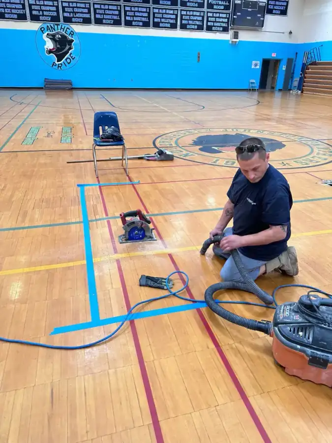 A Clean Care crew member repairing a high school gymnasium floor with power tools